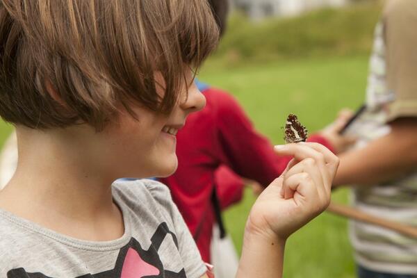 M�dchen mit langen braunen Haaren im Profil l�chelt und h�lt braunwei�er Schmetterling auf ihrem Finger.