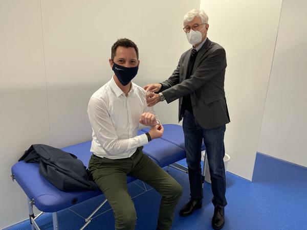 Landrat Andreas M�ller sitzt auf einer blauen Behandlungsliege und simuliert gemeinsam mit Dr. Thomas Gehrke, medizinischer Leiter des Impfzentrums, wie eine Corona-Impfung ablaufen wird. Sie befinden sich in einer der wei�en Kabinen im neuen Impfzentrum und tragen beide eine Mund-Nasen-Bedeckung.