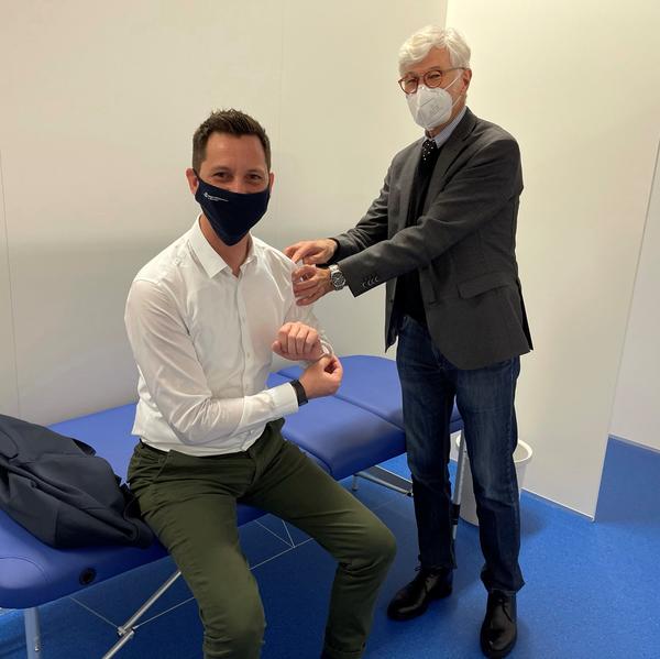 Landrat Andreas M�ller sitzt auf einer blauen Behandlungsliege und simuliert gemeinsam mit Dr. Thomas Gehrke, medizinischer Leiter des Impfzentrums, wie eine Corona-Impfung ablaufen wird. Sie befinden sich in einer der wei�en Kabinen im neuen Impfzentrum und tragen beide eine Mund-Nasen-Bedeckung.
